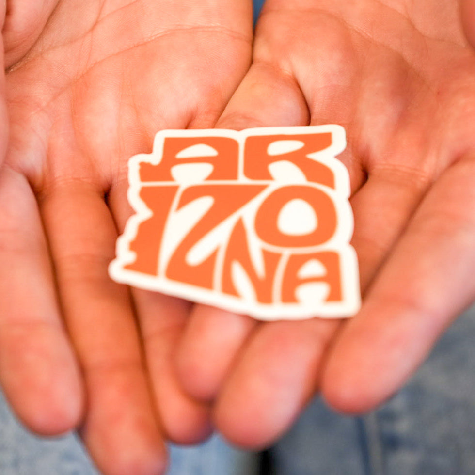 A hand holding a vinyl die cut sticker with the word 'ARIZONA' written in bold letters.
