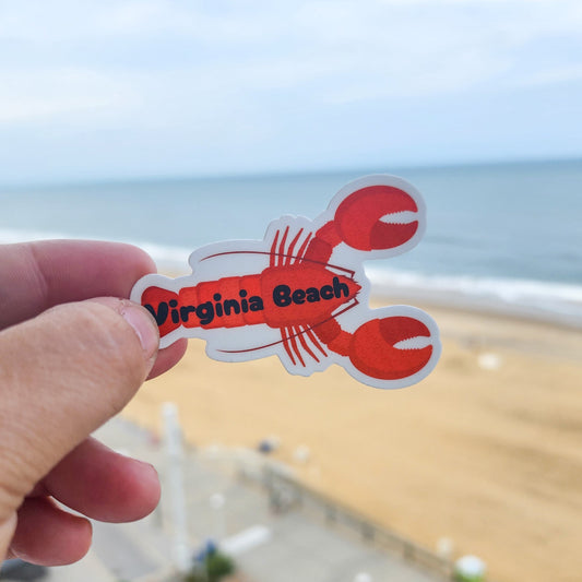 Red 'Virginia Beach' lobster sticker held up with a beach in the background