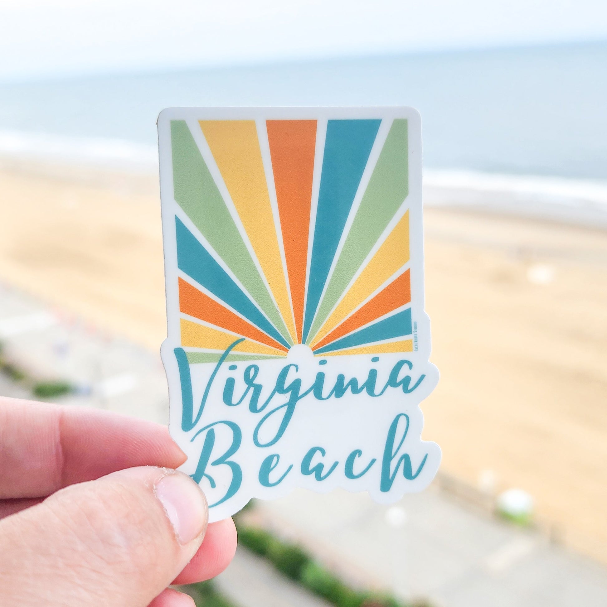 Colorful 'Virginia Beach' sticker held in front of a beach background