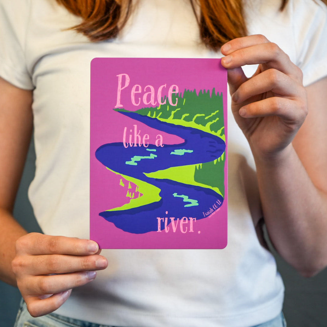 Person holding a card with a colorful design and text 'Peace like a river' against a neutral background