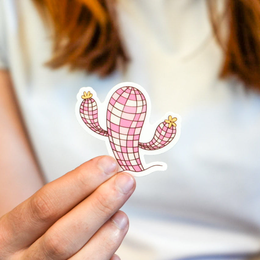 A vinyl die cut sticker of a pink grid patterned cactus held between fingers.