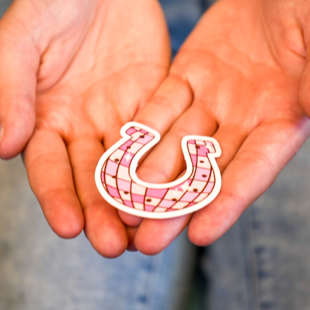 A vinyl die cut sticker in the shape of a horseshoe with a geometric pattern, held in two hands.